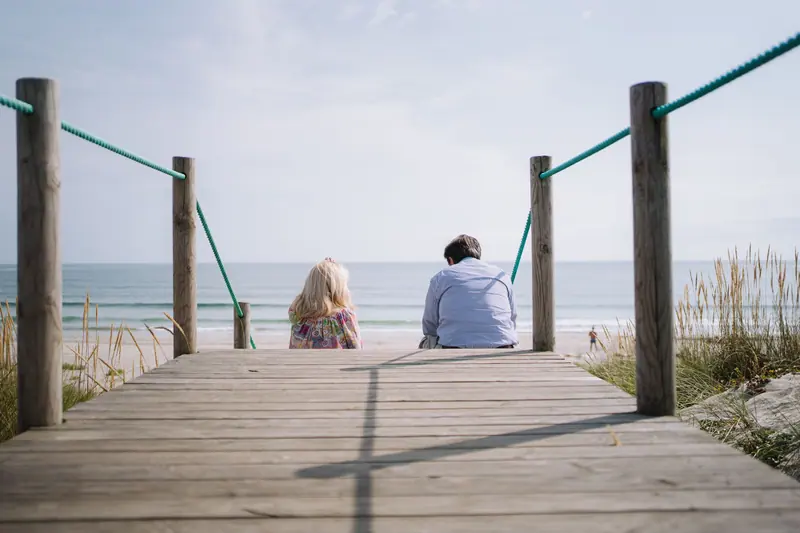 A couple enjoying a peaceful moment on a wooden boardwalk by the sea.