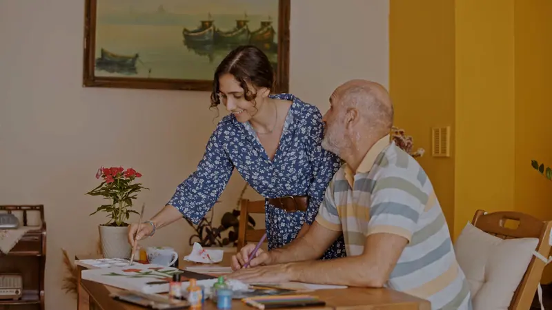 An elderly man and a woman enjoy a painting session together at a cozy indoor setting.