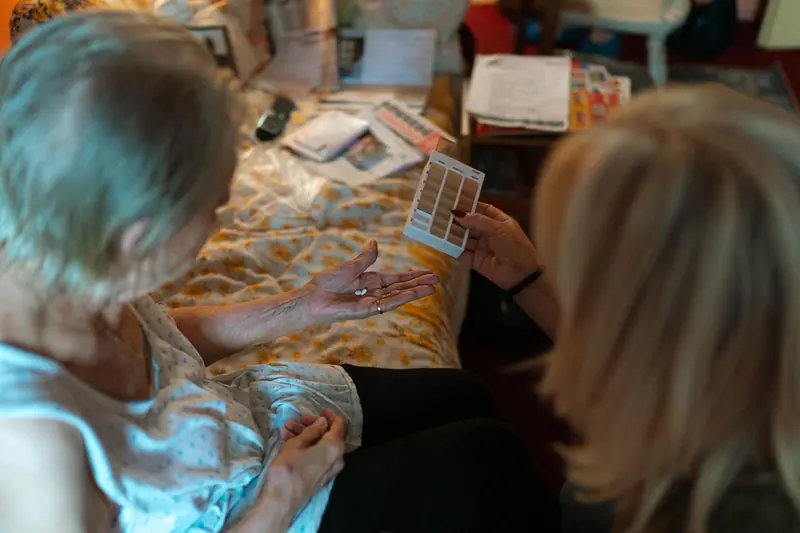 A nurse going through an older woman's pill organizer with her at the bedside