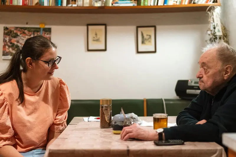 A young caregiver and an older man talking over tea at the kitchen table
