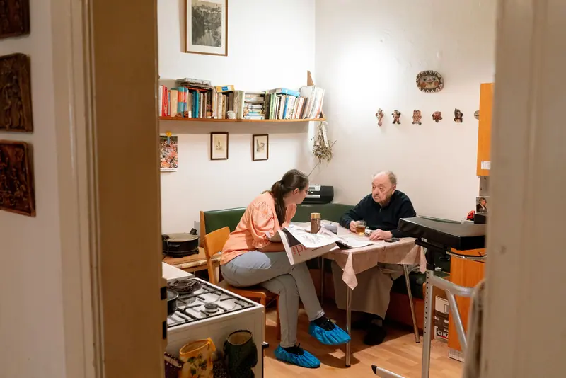 A caregiver and an older man talking over coffee at the kitchen table