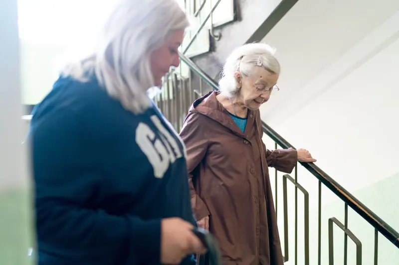 A caregiver beside an older woman practicing the stairs
