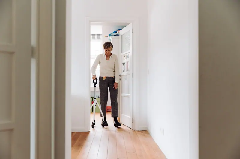 An older woman walking with her rollator down a bright hallway