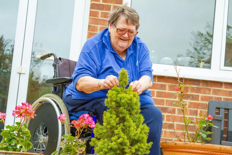 A resident in her wheelchair tending potted plants on the patio
