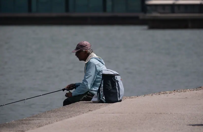 A man fishing from the seawall on a calm afternoon