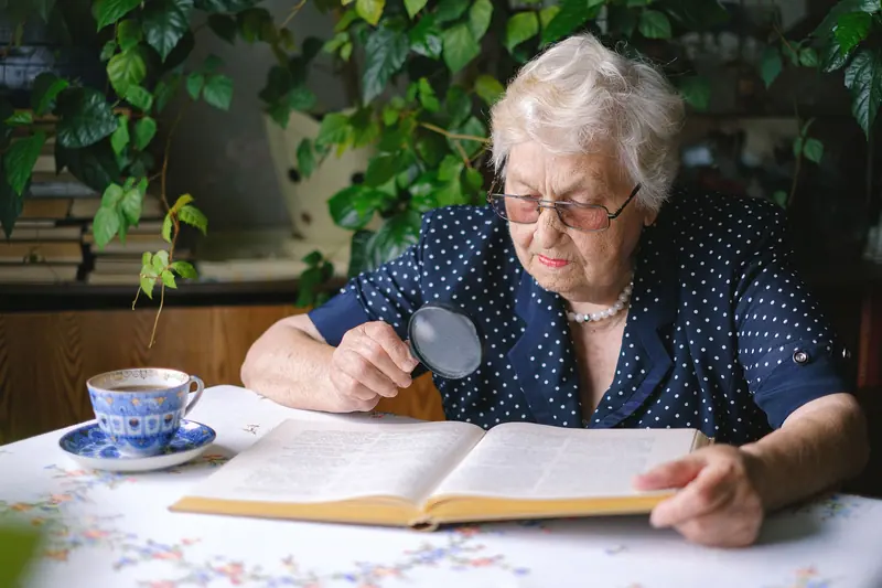 An older woman reading with a magnifying glass among her plants