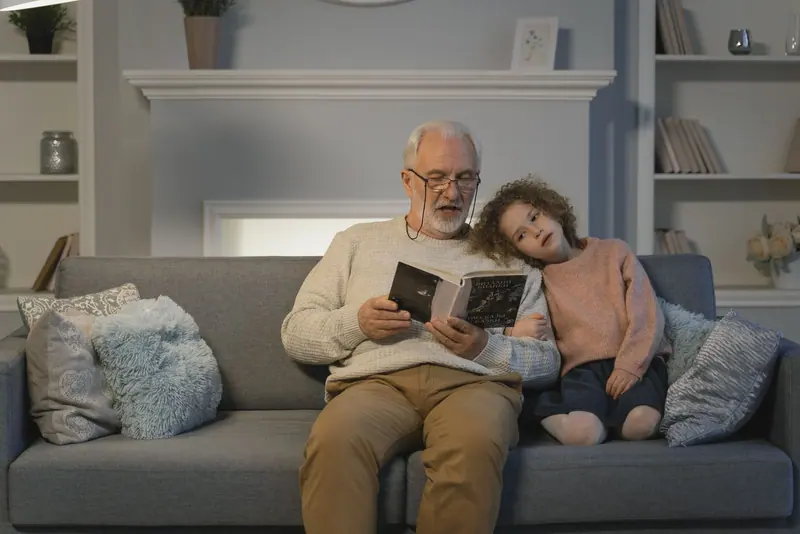 A grandfather reading on the sofa with his granddaughter