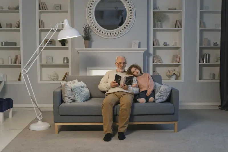 A grandfather reading to his granddaughter in the living room
