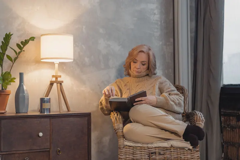 An older woman reading in her armchair by lamplight