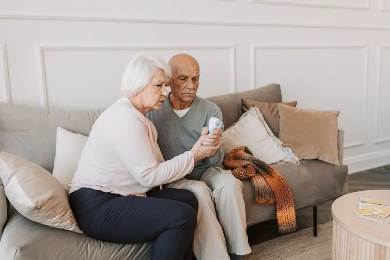 An older woman checking her husband's oxygen reading on their sofa