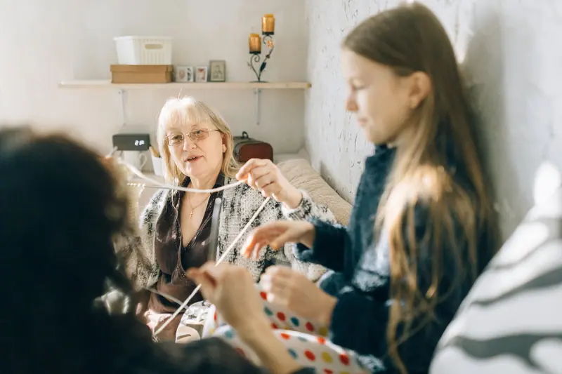 An older woman knitting with her granddaughters