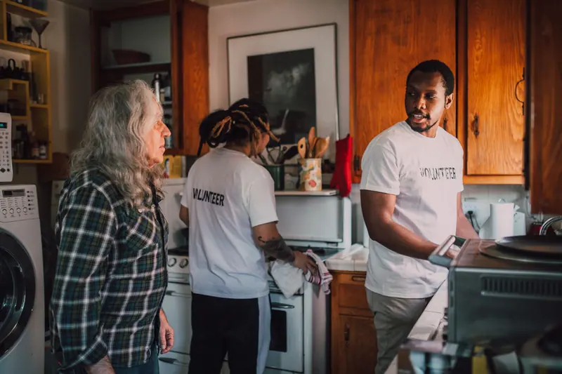 Aides helping an older woman put groceries away in her kitchen