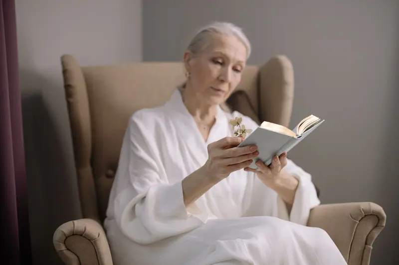 An older woman reading in a wingback chair