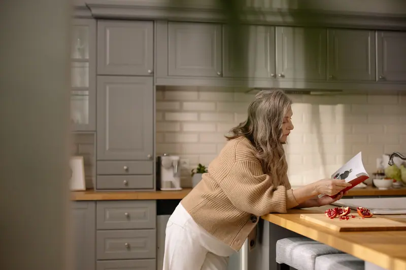 An older woman reading a recipe at the kitchen counter