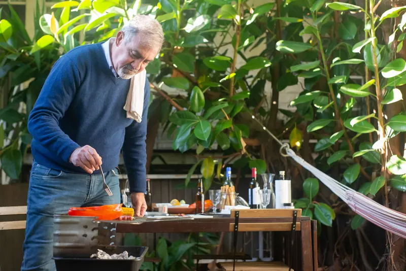 An older man grilling supper in his leafy backyard