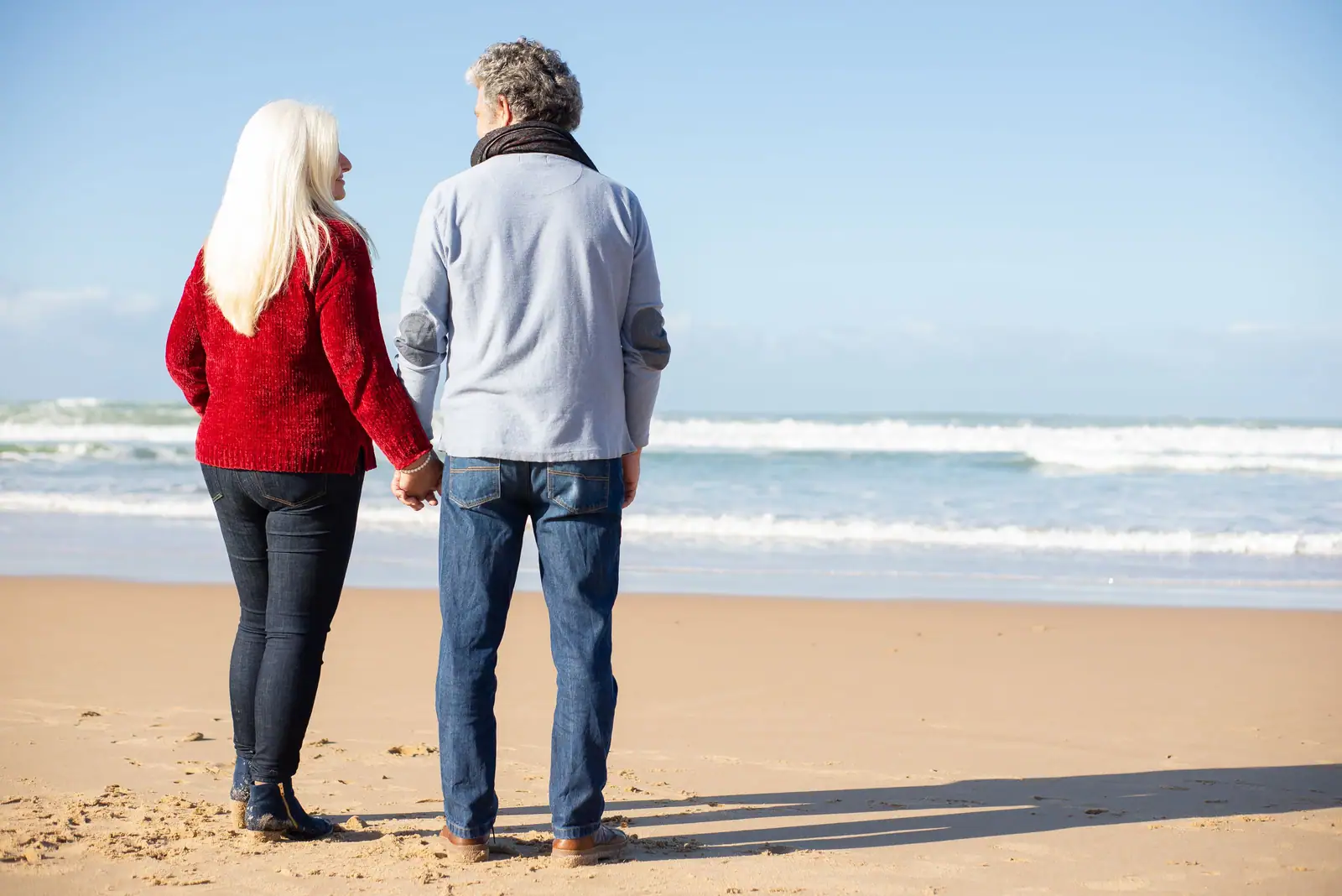 An older couple holding hands at the water's edge on a bright morning