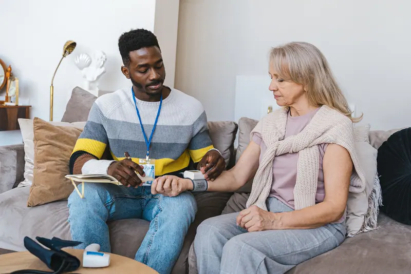 A nurse taking a woman's blood pressure on her living-room sofa