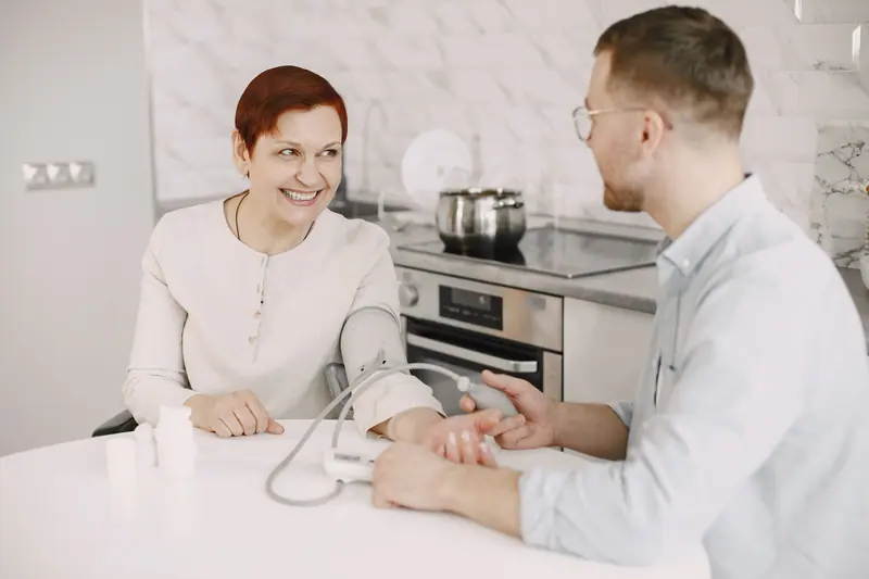 A nurse checking a woman's blood pressure at her kitchen table