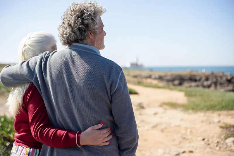 An older couple embracing by the water, looking out at the bay