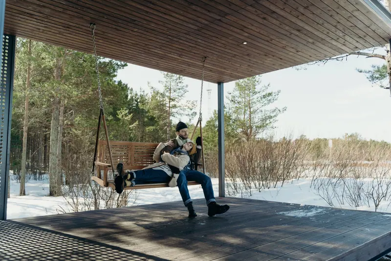 A couple enjoys a peaceful moment on a wooden swing amidst a snowy forest landscape.