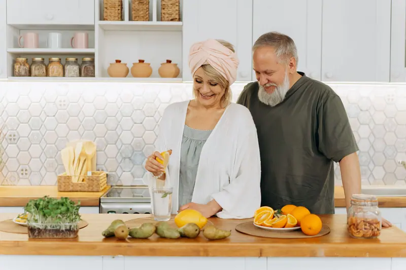 An older couple squeezing fresh citrus at their kitchen counter