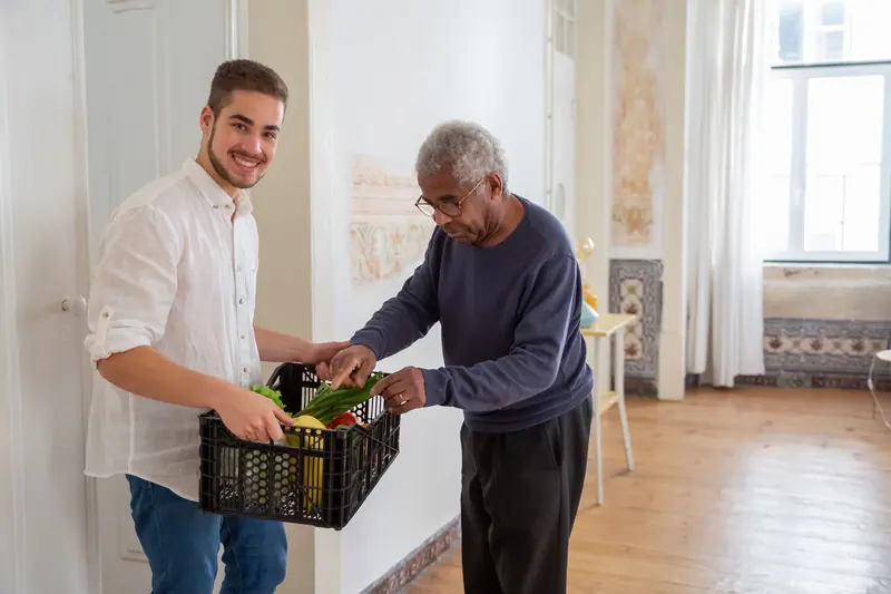 A young aide handing an older man a crate of groceries