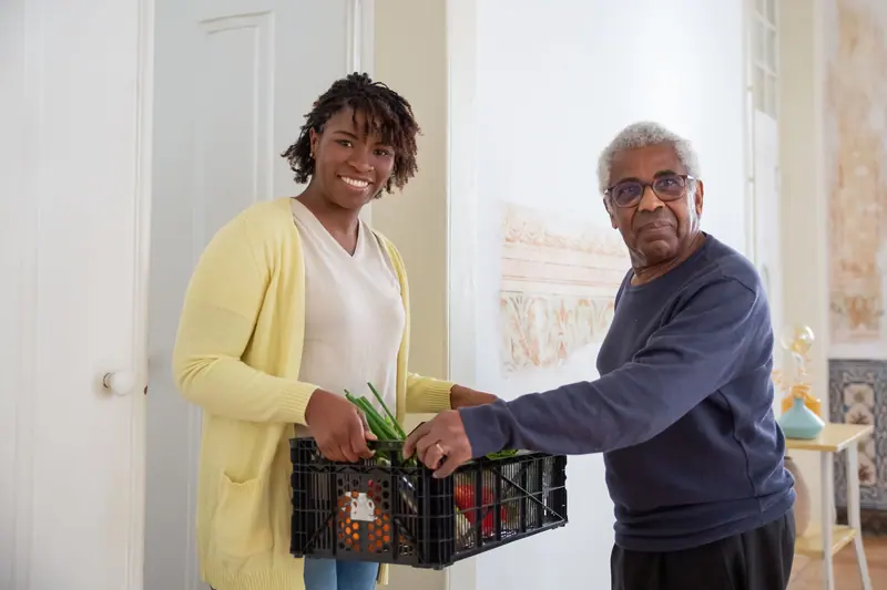 An aide bringing a crate of groceries to an older man's door