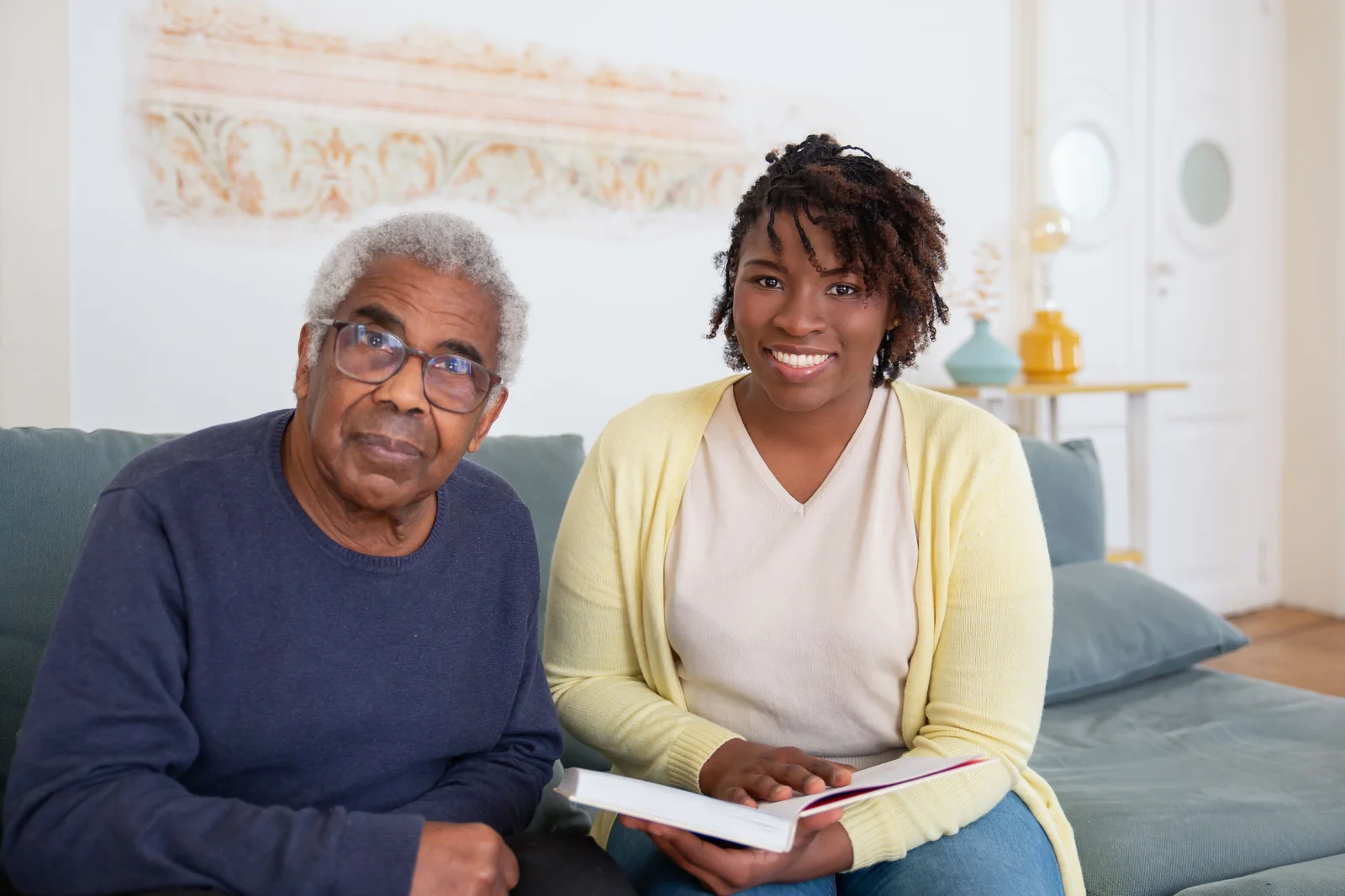 A caregiver and an older man smiling together on the couch