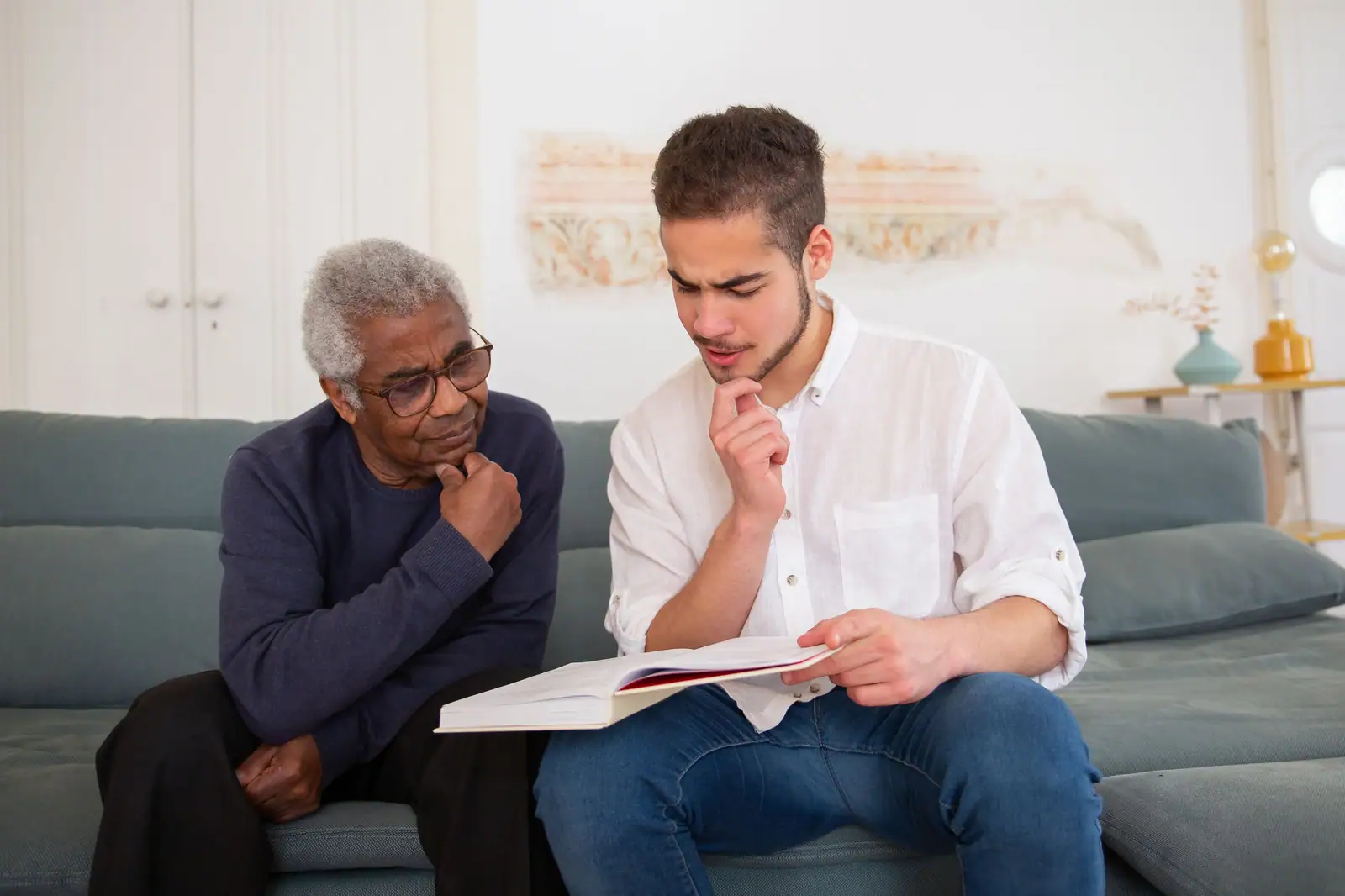 A young caregiver and an older man reading through paperwork on the sofa