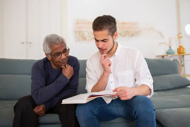 A young caregiver and an older man reading through paperwork on the sofa
