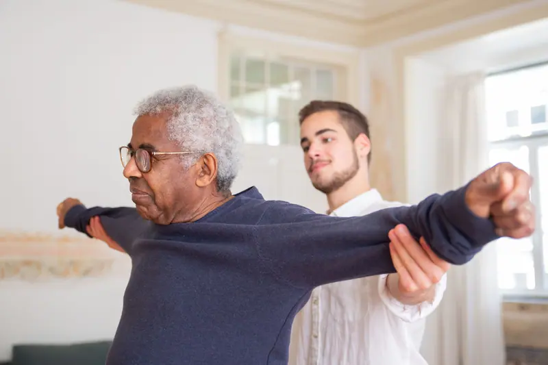 A therapist guiding an older man through shoulder stretches