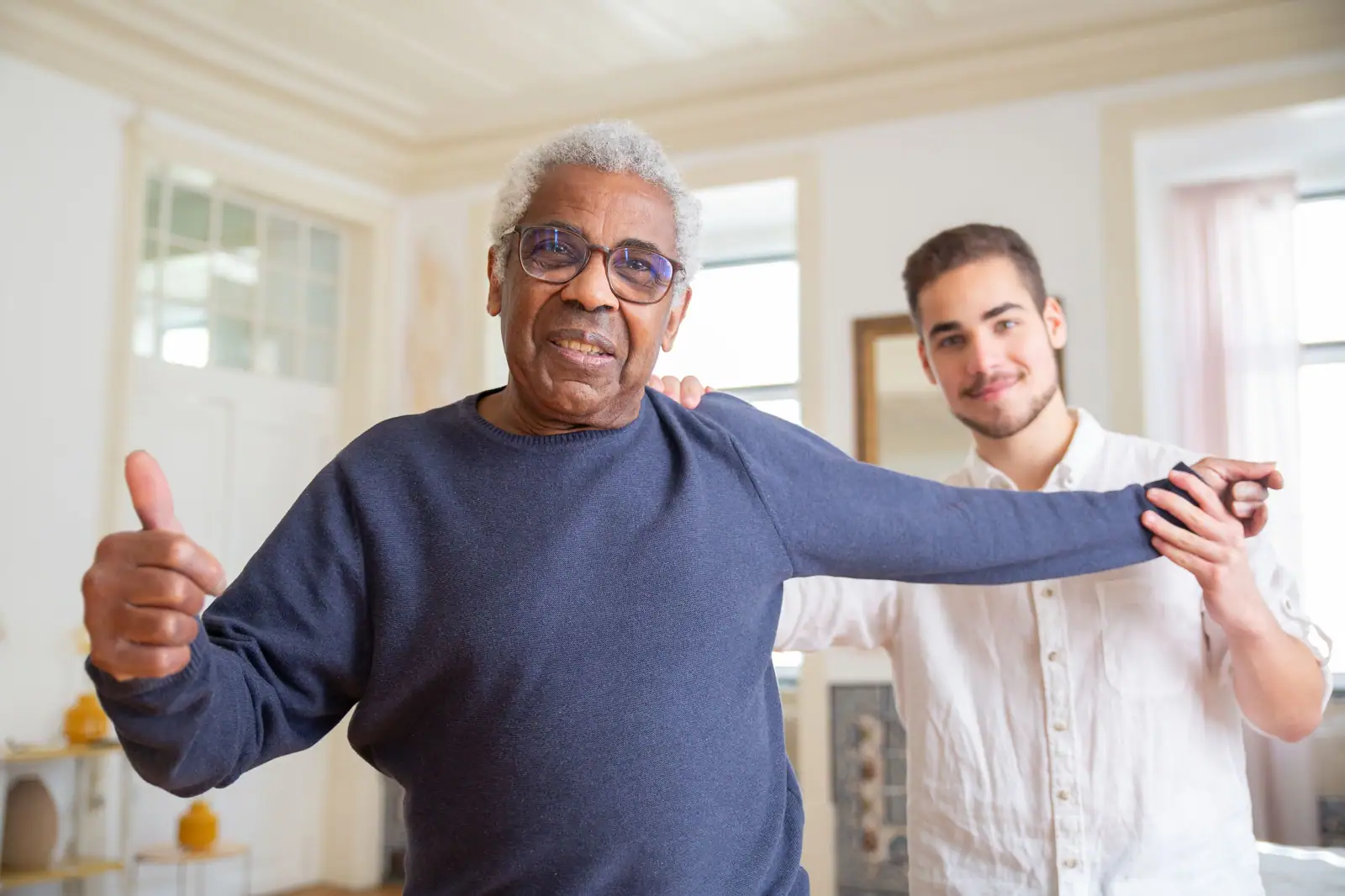 A home health therapist and a smiling older man doing arm exercises in his living room