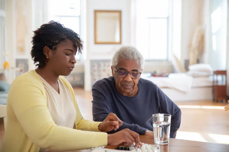 A nurse going over medications with an older man at his dining table