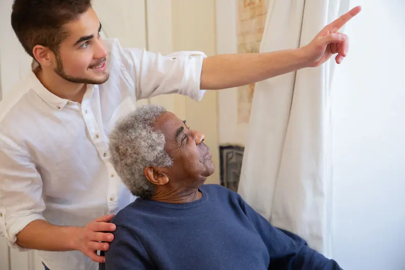 A therapist pointing out the window as an older man stretches in his chair
