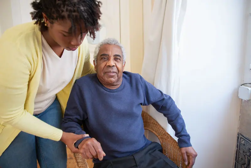 A home health nurse helping an older man settle into his chair after his first walk