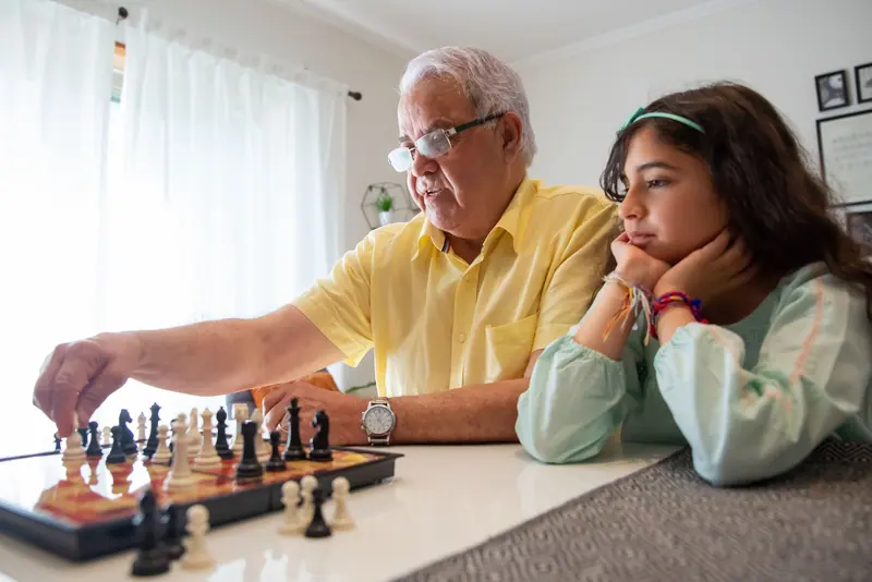 A grandfather playing chess with his granddaughter