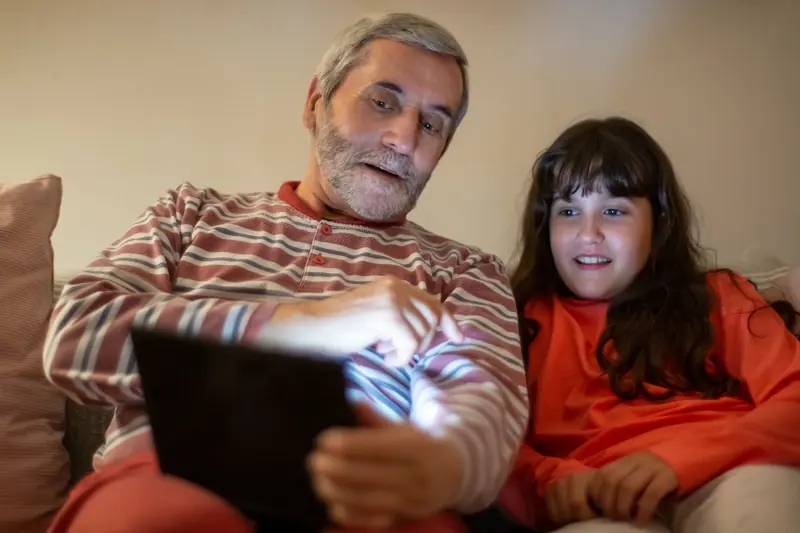 A grandfather and granddaughter watching something on a tablet