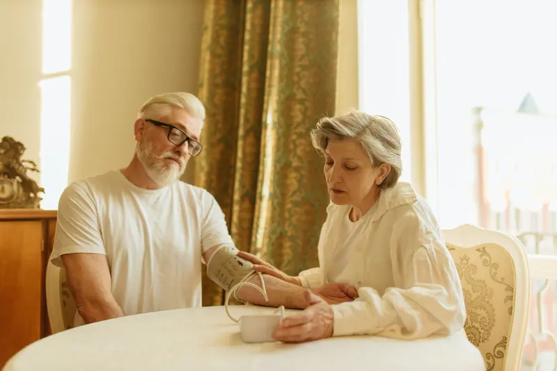 An older woman taking her husband's blood pressure at a round table