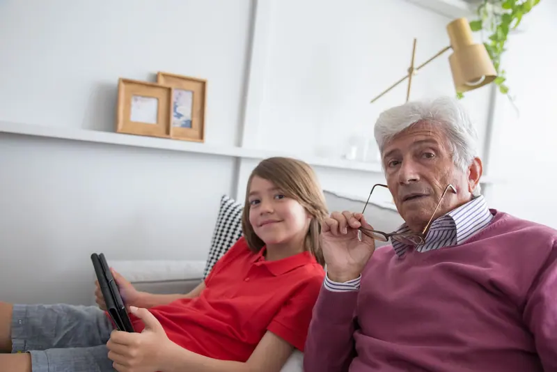 A grandfather and granddaughter sharing a tablet on the sofa