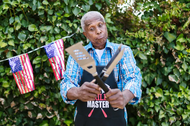 A resident in his Grill Master apron holding the spatula at the Fourth of July cookout