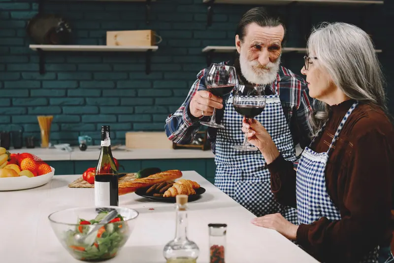 An older couple toasting each other while cooking dinner