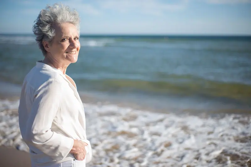 A smiling older woman standing in the surf in a white shirt