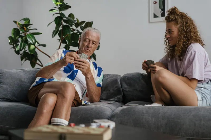 An older man and his granddaughter playing cards on the couch
