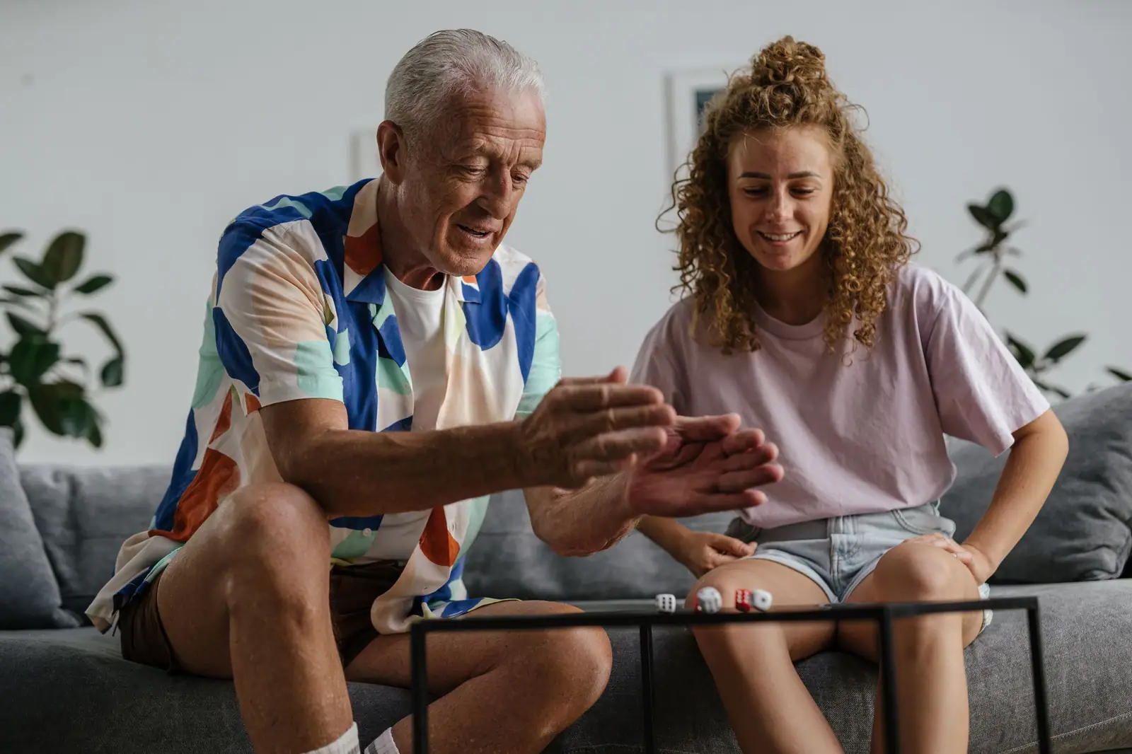 An older man laughing with his granddaughter over a card game on the living-room sofa