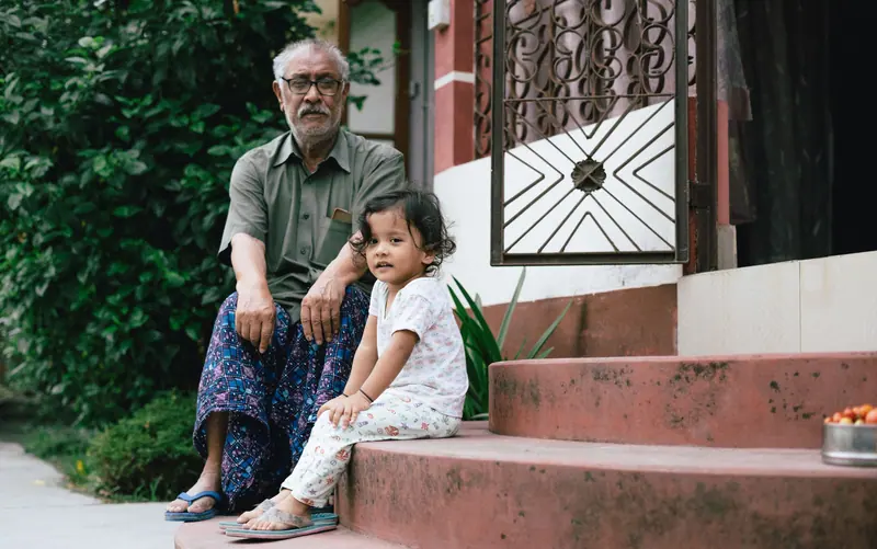 A grandfather sitting with his toddler granddaughter on the front steps