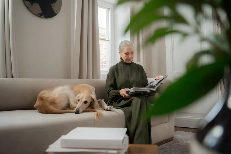 A woman reading with her dog curled up on the couch