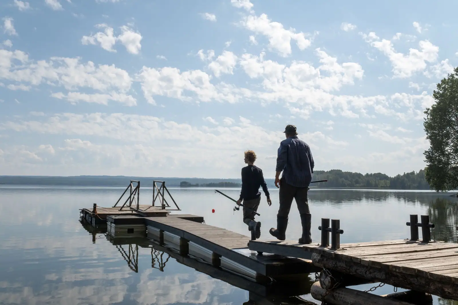 A grandfather and his grandson walking out onto the dock over still water on a bright morning