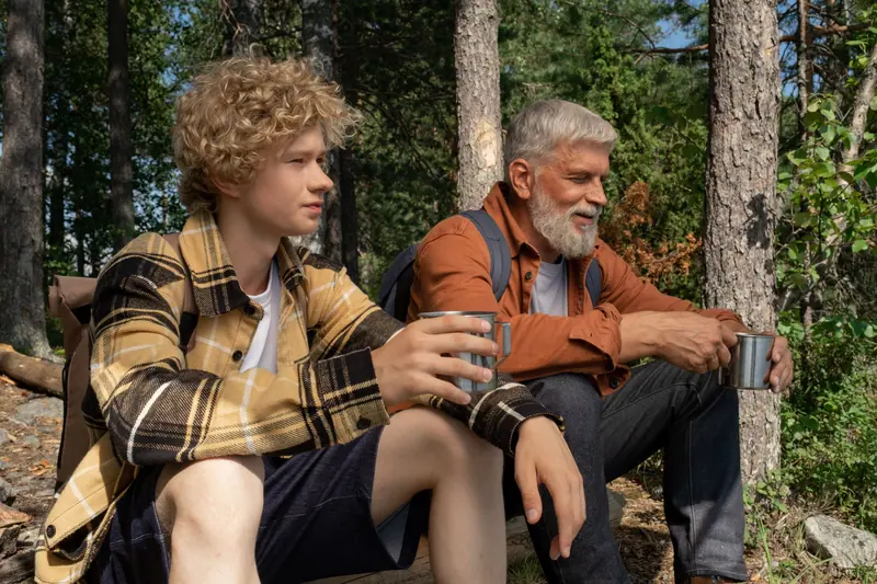 A grandfather and grandson resting with coffee on a forest walk