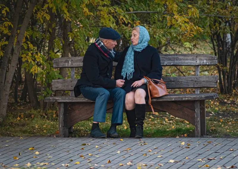 A married couple sitting close on a park bench in fall
