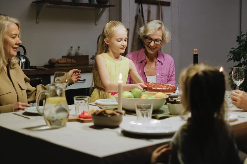 A grandmother and her granddaughters passing dishes around the supper table